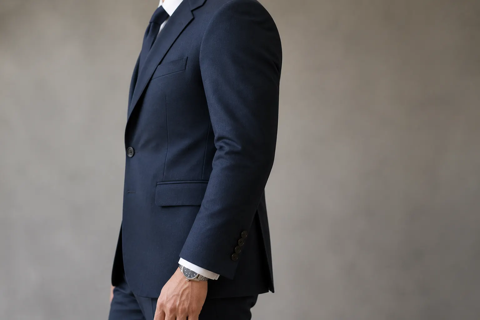 Side view of a navy suit jacket shoulder and sleeve with a small amount of white shirt cuff showing at the wrist